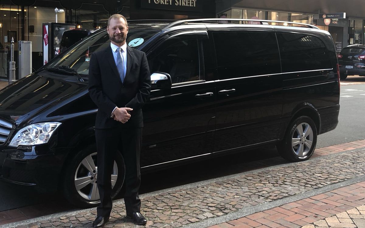 Mike in a suit beside his black Mercedes V350 on a Wellington street