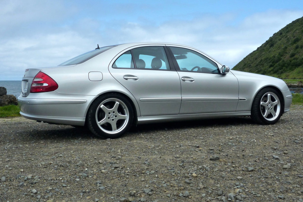 Ein silberner Mercedes E500, auf Schotter geparkt, unter offenem Himmel